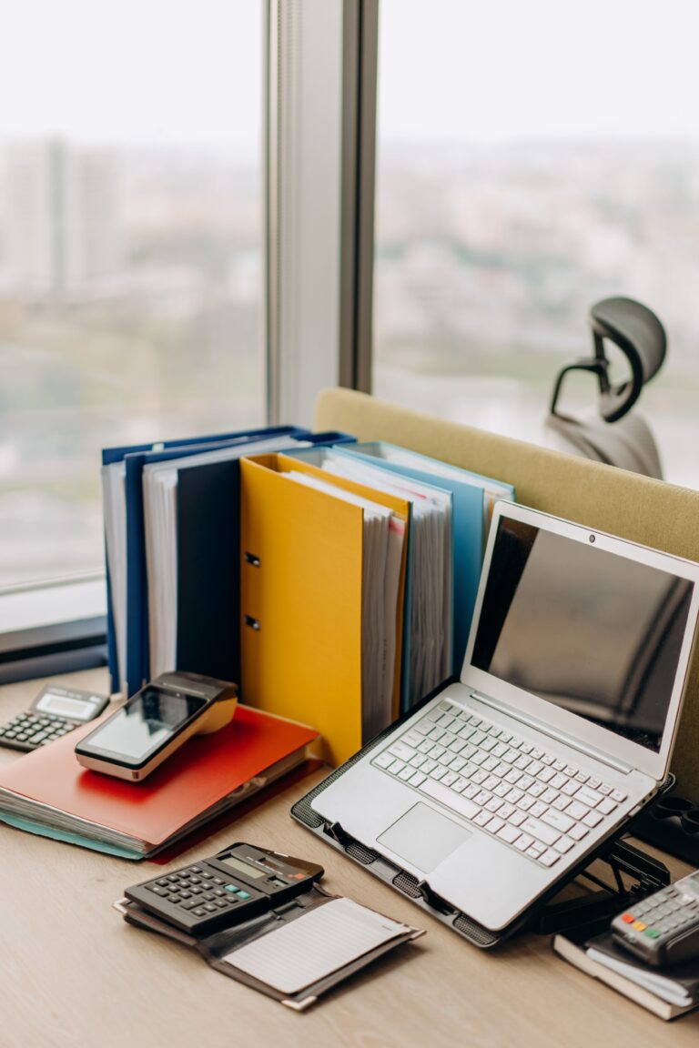 Cadeau d'entreprise original et personnalisé 46 Bureau en bois, sur lequel est posé des classeurs de travail, un petit ordinateur portable et une calculatrice