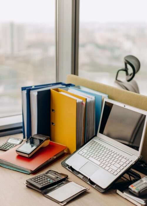 Bureau en bois, sur lequel est posé des classeurs de travail, un petit ordinateur portable et une calculatrice