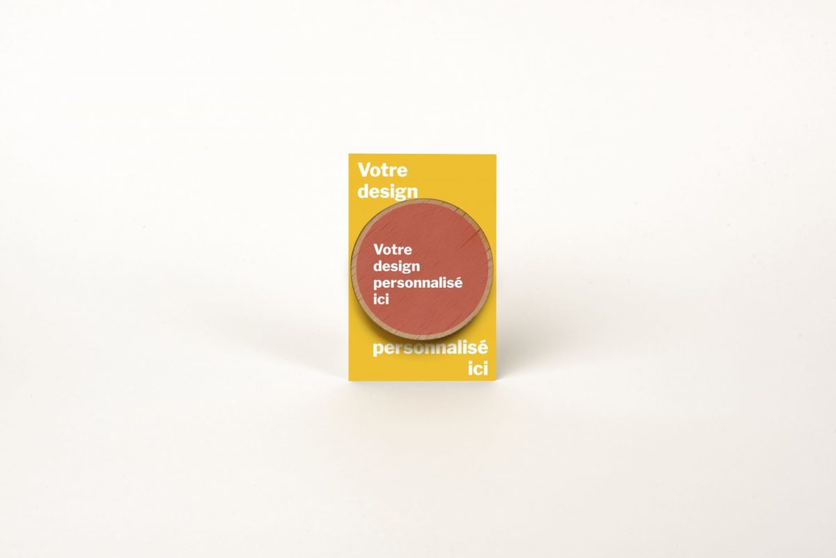 Un petit paquet avec une étiquette jaune, contenant un Badge rond (pins) en bois et français (S,M ou L) - Aimant.