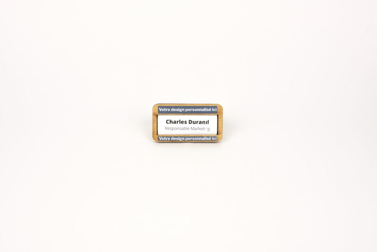 Un petit badge rectangle en bois et français avec une étiquette posée sur une surface blanche.