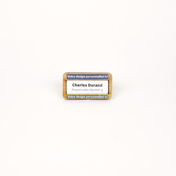 Un petit badge rectangle en bois et français avec une étiquette posée sur une surface blanche.