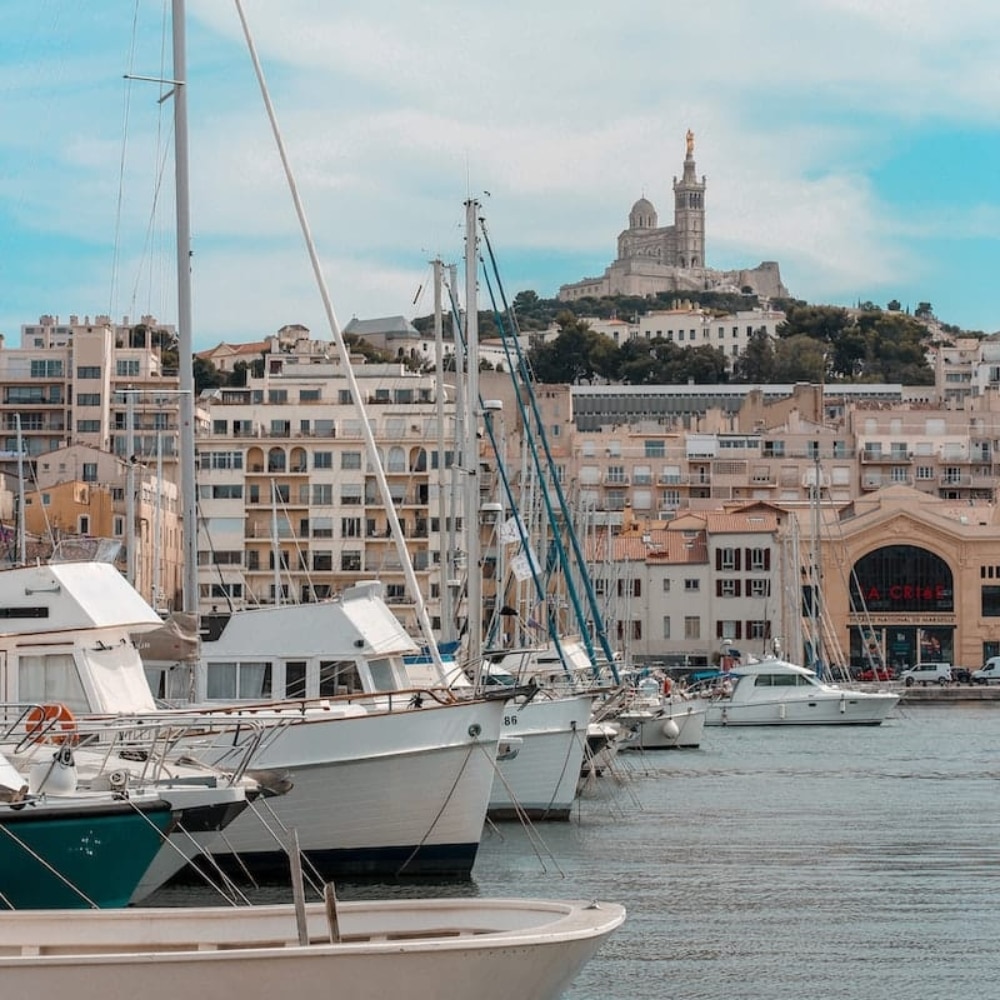 Bateaux amarrés dans un port avec une ville en arrière-plan, avec des pains de savon Petit Savon de Marseille Olive.