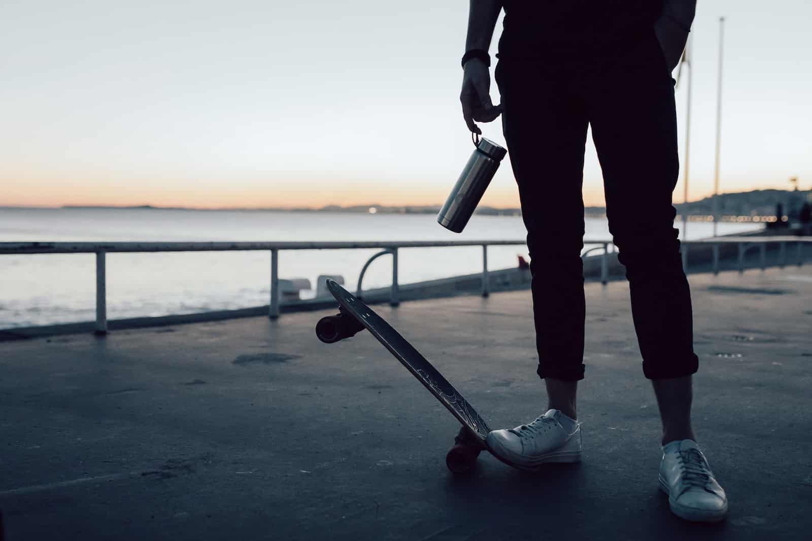 homme faisant du skateboard avec une gourde isotherme