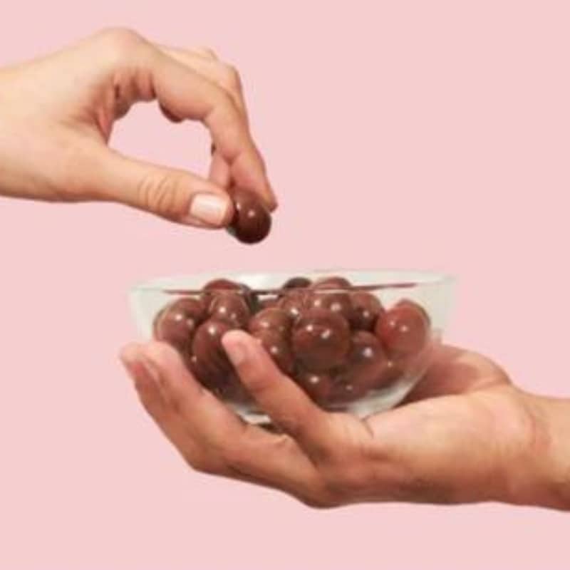 Deux mains cherchant des billes soufflées enrobées de chocolat dans un bol.