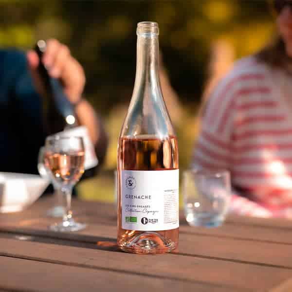 Une bouteille de Vin Rosé - Grenache 2021 IGP pays d'Oc, élaborée à partir de raisins grenache, repose sur une table en bois.