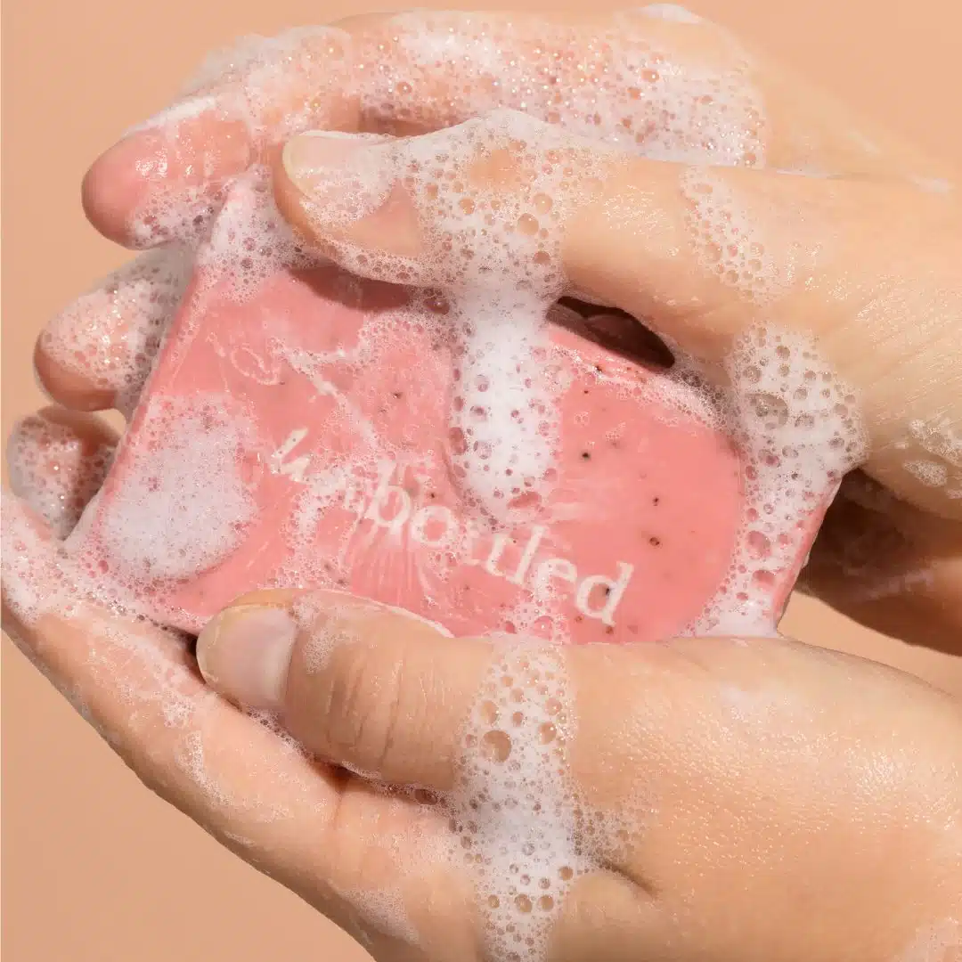Une personne se lave les mains avec un savon Mains-Toutes-Douces rose.