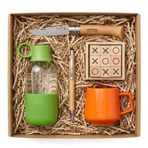 Visuel d'un coffret en kraft rempli de frisures, avec quelques produits disposés à l'intérieur : une gourde, un mug, un jeu de morpion, un couteau